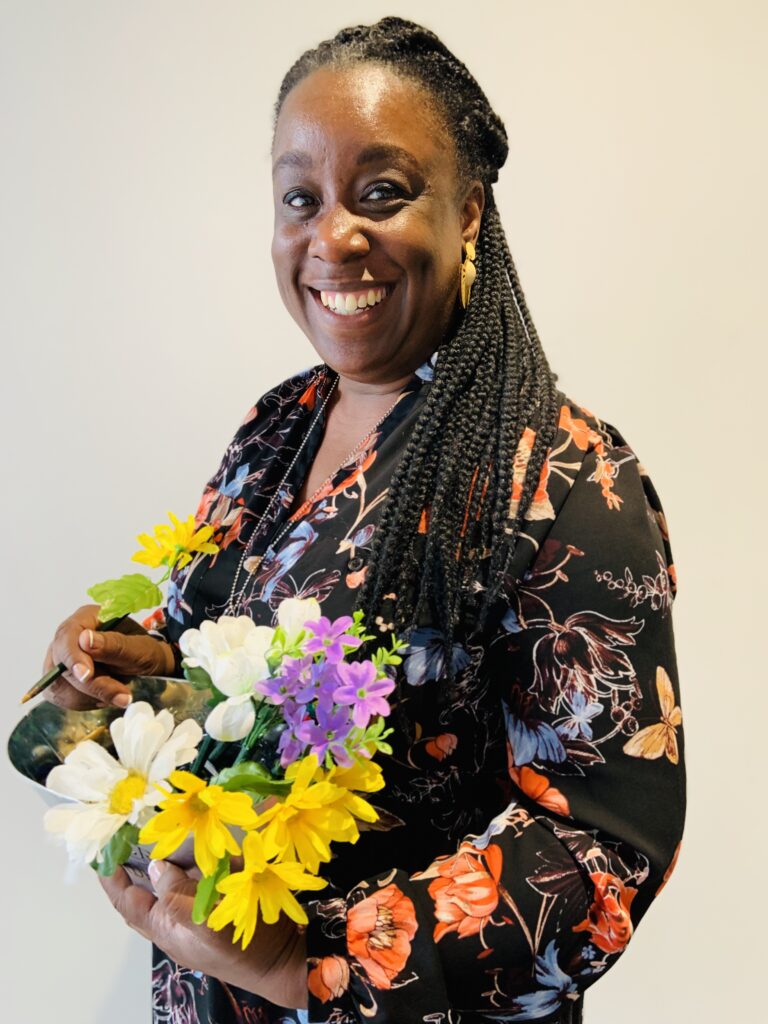 MsTmusze smiling wearing a flowered dress holding a bouquet of flower pens